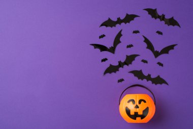 Cadılar Bayramı süslemelerinin en üst görüntüsü kabak sepetinden boşluklu mor arka planda uçan büyük ve küçük yarasalar