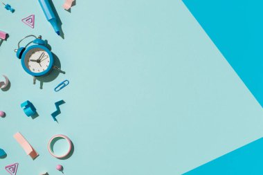 Kompozisyon kırtasiyesinin üst görüntüsü bicolor mavi ve pembe okul malzemeleri bağlayıcı raptiye yapışkan bant ve alarm saati izole edilmiş pastel mavi arkaplan