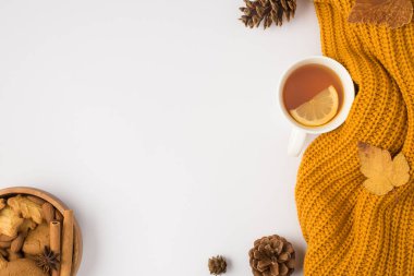 Sarı örülmüş çay fincanının üst görüntüsü limon sarısı sonbahar yaprakları kozalaklı ve çerezli kase badem fıstıklı anason ve tarçın çubuklarıyla izole edilmiş beyaz arka planda