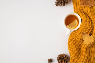Sarı örülmüş çay fincanının üst görüntüsü. Limon sarısı sonbahar yaprakları ve kopyalanmış beyaz arka planda çam kozalakları.