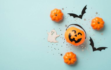 Cadılar Bayramı süslemelerinin en üst görüntüsü balkabağı sepeti gümüş pullar yarasa ve hayalet siluetleri izole edilmiş pastel mavi arka planda