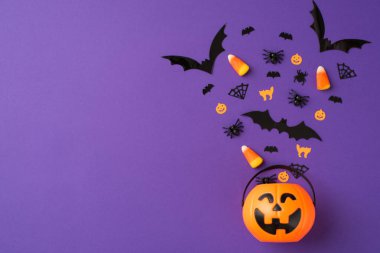 Cadılar Bayramı süslemelerinin en üst görüntüsü yarasalar örümcekler ağ mısır şekeri kediler balkabağı siluetleri kabak sepetinden uçuyor izole edilmiş menekşe arkaplanı boş.