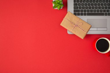 Gri dizüstü bilgisayarında sicim yayı olan dikdörtgen el işi kağıt hediye kutusu ve izole edilmiş kırmızı arka planda bir fincan kahve.