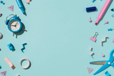 Bicolor mavi ve pembe okul aksesuarlarının üst görüntüsü kalemlerin bağlayıcı raptiyelerin yapışkan bant makası ve izole edilmiş açık mavi arkaplanda alarmlı saatin ortasındaki kopya boşluğu hissetti.