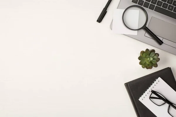 Top view photo of magnifying glass sticker note on grey laptop pen plant and glasses on two notebooks on isolated white wooden table background with copyspace