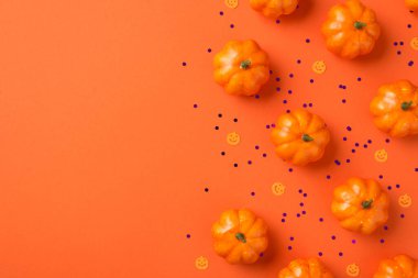 Cadılar Bayramı süslemelerinin üst görüntüsü küçük balkabağı siluetleri ve izole edilmiş turuncu zemin üzerindeki mor pullar kopyalanmış