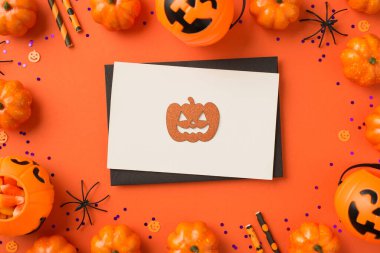 Siyah zarfın en üstteki fotoğrafı portakal rengi balkabağı oymalı siluet beyaz kart menekşe rengi pullar balkabağı sepetleri şeker mısır örümcekleri ve izole edilmiş turuncu arka planda pipetler.