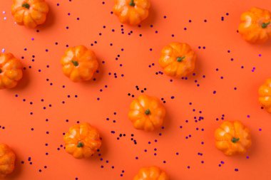 Cadılar Bayramı süslemelerinin en üst görüntüsü izole edilmiş turuncu arka planda küçük balkabakları ve menekşe konfetileri