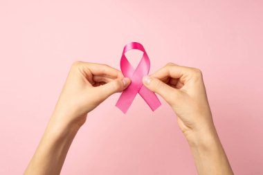 Göğüs kanserinin sembolü olan pembe saten kurdeleli ellerin izole edilmiş pastel arka planda görüldüğü ilk kişi.