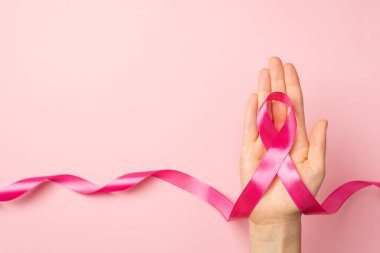 Avuç içi kanserinin sembolü olan pembe kurdeleli bir kadının, izole edilmiş pastel pembe arkaplanlı ve kopyalanmış pembe renkli bir el resmi.