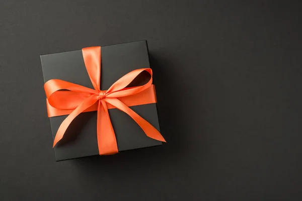 带有橙色缎带蝴蝶结的黑色礼品盒的顶部照片 独立的黑色背景 有彩色空间 — 图库照片