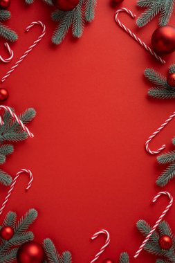 Kırmızı arka planda şeker kamışı ve çam dalları bulunan dikey tatil sınırı, Noel ve yeni yıl kutlamaları ve terfileri için mükemmel.