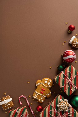 Neşeli bir tatil sahnesi, gülümseyen bir zencefilli çörekçi, hediye paketleri, şeker kamışları, süsler ve yıldız konfetileri, sıcak kahverengi bir arka planda ayarlanmış, Noel ve yeni yıl ruhunu yakalıyor.