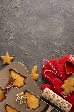 Yıldız şekilli kurabiyeler, metal kesici kalıplar, şeker kamışları, kırmızı kumaş ve bayram kutlamaları için şenlikli dekorlar içeren dikey, sıcak bir Noel pişirme seti.