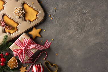 Samimi bir Noel pişirme sahnesinde metal tepside kesme kurabiyeler, kırmızı bir çek kurdelesi, çam dalları, böğürtlen ve şeker kamışları ile bağlanmış bir hediye kutusu, tatil sıcaklığını yakalıyor.