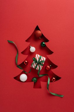 Süslerle dolu biçimlendirilmiş bir Noel ağacı kesimi ve yeşil kurdeleyle bağlanmış çizgili bir hediye, şenlik havasını yakalayan, hediye veren ve bayram neşesi veren kırmızı bir arka plan.