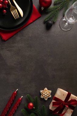 Kırmızı peçete, siyah tabak, altın çatal bıçak, mumlar, çam dalları, süsler, paketlenmiş bir hediye, bir kar tanesi kurabiyesi ve yılbaşı ve yeni yıl kutlamaları için hazır bir şarap kadehinden oluşan dikey bir daire.