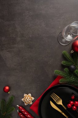 Koyu bir üst görünüm dikey arkaplan, kırmızı peçete, yemyeşil filizler, kırmızı böğürtlenler, kar tanesi süsü ve bayram tostu için hazır zarif altın çatal bıçaklarla dolu bir Noel masası sahnesini çerçeveler.