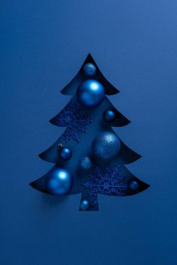 Metalik süsler ve kar taneleriyle süslenmiş dikey mavi bir Noel ağacı.