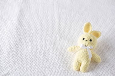 Beyaz kurdeleli rahat sarı örülü tavşan pelüşü beyaz desenli bir battaniyenin üzerinde duruyor. Yeni doğan fotoğrafçılığı, bebek hediyeleri ve annelik hatıraları için mükemmel.