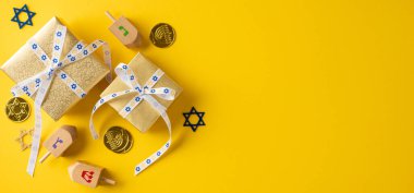 Canlı Hanuka bayrağı hediyeleri, bir dreidel, jöleli sikkeler ve cesur sarı bir arkaplan karşısında David motifli bir yıldız, festival geleneğini ve hediye değişimi enerjisini yansıtıyor.