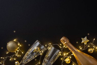 İki kristal bardak, parıldayan ışıklar ve altın süsler ile eşleştirilmiş zarif şampanya şişesi Noel ve yeni yıl kutlamaları ve kutlamalar için mükemmel bir şenlik havası yaratır.