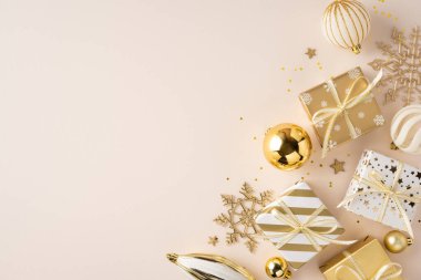 Yumuşak bej arka planda, Noel ve yeni yıl kutlamaları için hazır altın sarısı hediyeler, süsler ve kar taneleri ön plana çıkıyor