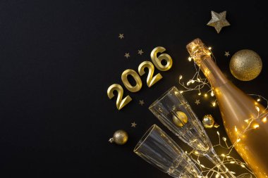 Noel ve yeni yıl kutlamaları için bir şampanya şişesi, iki kristal bardak, sicim lambaları ve altın süslemeler, 2026 için ışıltı, sıcaklık ve şenlik neşesinin yer aldığı büyüleyici bir bayram anıdır..