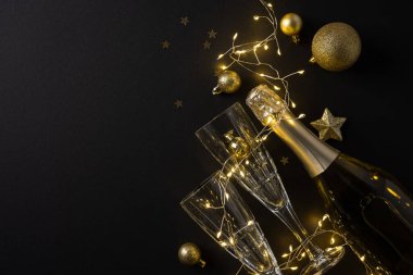 Şampanya şişesinin kristal flütlere döküldüğü, ışıkların yanıp söndüğü ve Noel ve yeni yılı kutlayan altın süslerle dolu bir sahne.