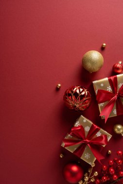 Kırmızı dikey arka plan, kırmızı kurdeleler ve altın süslerle paketlenmiş hediyeler, Noel ve Yeni Yıl kutlamalarını çağrıştırıyor ve bayram kutlamalarını şenlikli cazibeyle ve sıcak mevsimsel havayla karşılıyor.