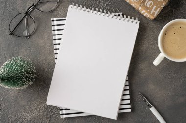 Çizgili kapaklar, bardaklar, küçük bir Noel ağacı, bir kupa kahve ve tatil notlarına hazır bir kalem ve yeni yıl dilekleri içeren boş bir defter.