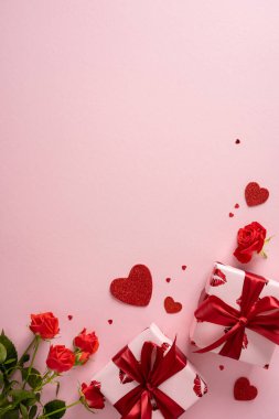 Kırmızı güllerin, kırmızı kurdelelerle bağlanmış hediye kutularının ve yumuşak pembe arka planda dağılmış kalplerin yer aldığı romantik bir dikey sahne. Sevgililer Günü terfileri ve temalı kartlar ya da projeler için mükemmel