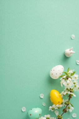 Paskalya yumurtaları ve beyaz çiçekler yumuşak, dikey bir arkaplanda dinleniyor. Paskalya kutlamaları, bahar promosyonları ve mevsimsel dekoratif tasvirler için ideal bir festival sahnesi oluşturuyor.