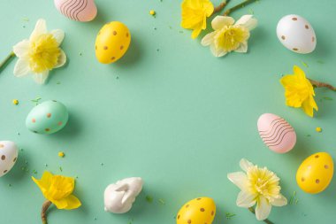 Renkli yumurtalar ve nane arkaplanda sarı nergislerle dolu canlı Paskalya sahnesi tebrik kartları ve bahar promosyonları için neşeli, neşeli bir ortam yaratır.