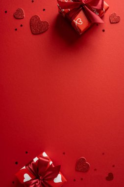 Parlak dikey kırmızı arkaplanda hediye kutuları, kurdeleler ve parıldayan kalpler, tebrik kartları, tanıtımlar ve romantik kampanyalar için ideal sıcak bir sevgililer günü havası yakalanıyor.