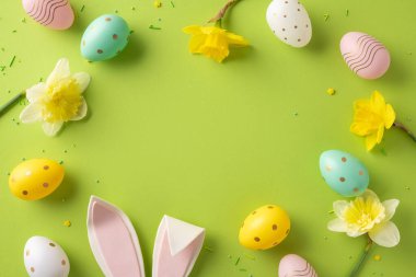 Pastel yumurta aksanlı parlak Paskalya sahnesi, sarı nergis çiçekleri, ve canlı yeşil arka planda yumuşak tavşan kulakları, bayram kutlamaları ve bahar kutlamaları için mükemmel.