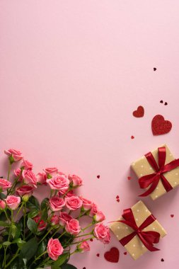 Pembe güller, kırmızı kurdelelerle bağlanmış hediye kutuları ve yumuşak pembe bir arkaplanda dağılmış kalpler içeren canlı, dikey sevgililer günü sahnesi sıcak bir romantik ortam yaratıyor.