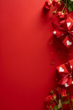 Güllerle dolu parlak kırmızı arka plan, kırmızı kurdele ve beyaz kalp desenlerine sarılı hediye kutuları, Sevgililer Günü teması ve romantik kutlama temaları için mükemmel.