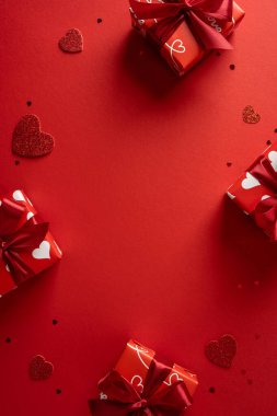 Hediye kutusu, kırmızı kurdele ve kalp aksanının yer aldığı romantik dikey sevgililer günü kurgusu aşk, kutlama ve tebrik kartları ve tanıtım kartları için uygun sevgi dolu anları çağrıştırmak için koyu kırmızı bir zemin hazırlıyor.