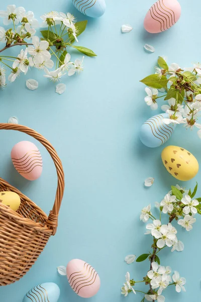 Pastel dikey Paskalya yumurtaları örülmüş bir sepetin içinde beyaz çiçeklerin ve taç yapraklarının arasında yumuşak mavi bir zemin üzerinde oturur ve Paskalya kutlamaları için şenlikli ve hoş bir sahne yaratır.