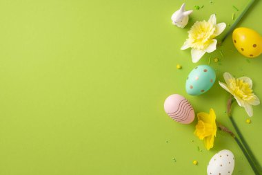 Canlı Paskalya sahnesinde pastel yumurtalar, neşeli çiçekler ve canlı yeşil arka planda neşeli bir tavşan seti var. Kutlama kartları ve bahar şenliği havasında mevsimlik terfiler için mükemmel.