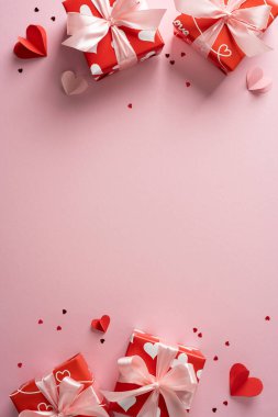 Kırmızı hediye kutuları, beyaz kurdeleler ve pembe arka planda dağınık kalplerle romantik dikey sevgililer günü sahnesi selamlama ve kutlama temaları için mükemmel.