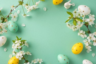 Canlı Paskalya yumurtaları nane yeşili bir zeminde beyaz çiçeklerin arasında otururlar. Bu şenlik düzeni bahar ve bayram neşesini yakalar, Paskalya kutlamaları, mevsimlik kampanyalar, kutlama görselleri için mükemmeldir.