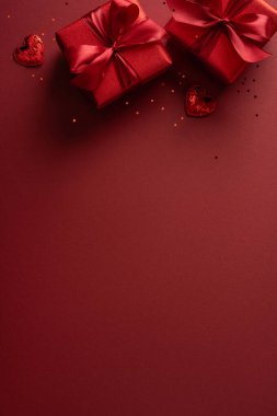 Kırmızı dikey sevgililer günü sahnesi paketlenmiş hediye kutuları, kurdeleler ve küçük kalpler romantizm, hediye alışverişi ve sevgililer günü terfileri ve selamlaşmaları öneriyor.