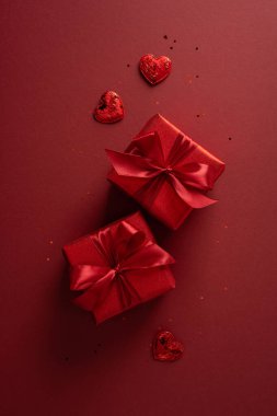 İki dikey kırmızı hediye kutusu saten kurdelelerle bağlanmış koyu kırmızı arka planda kalp çikolatalarının arasında oturur, hediyeler, tebrik kartları ve şenlikli promosyonlar için mükemmel romantik bir sevgililer günü sahnesi yaratır.