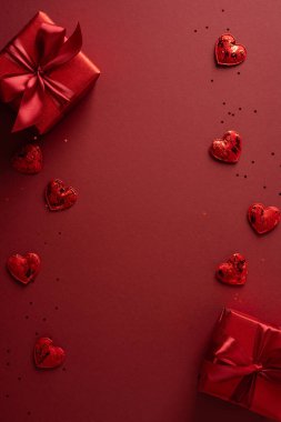Romantik dikey kırmızı arka plan gösterileri hediye kutuları ve dağınık kalpler paketledi. Kutlamalar, selamlar, hediyeler ve romantik etkinlikler için mükemmel bir sevgililer günü havası yarattı.
