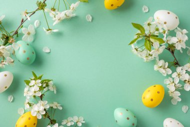 Pastel Paskalya yumurtaları, yumuşak yeşil bir arka planda beyaz çiçeklerin arasında oturur, bahar kutlamaları ve sıcak selamlar için mükemmel, parlak, şenlikli bir sahne yaratır.