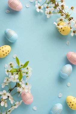 Pastel dikey Paskalya yumurtaları narin mavi bir fon üzerinde narin beyaz çiçeklerin arasında süzülür. Bahar cazibesini ve şenlik enerjisini yakalar. Selamlar, mevsimsel dekorlar ve terfiler için mükemmeldir.