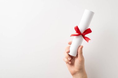 Kırmızı kurdeleyle bağlanmış bir diplomayı tutan bir el, mezuniyeti, başarıyı ve temiz bir stüdyo ortamının gelecek planlarını sembolize ediyor.