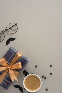 Babalar Günü için canlı, dikey bir hayat. Turuncu kurdeleli ekose bir hediye kutusu, kahve fincanı, erkeksi ve düşünceli bir kutlama için bardaklar ve bıyıklar.